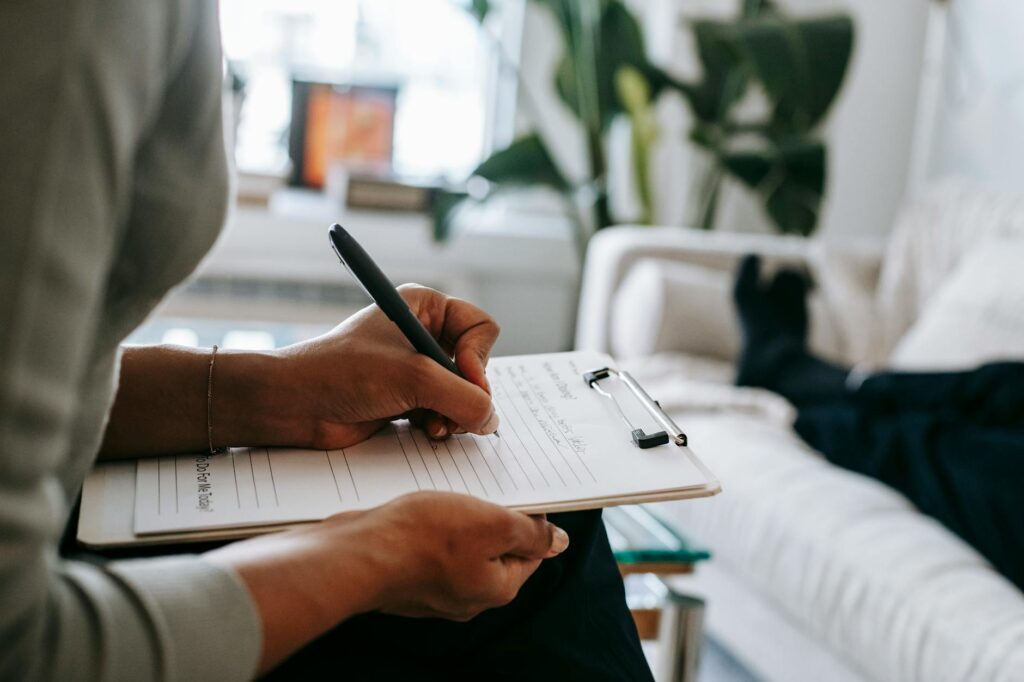 crop ethnic psychologist writing on clipboard during session - depression CBT